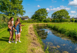 En familie nyder naturen ved en lille sø i en feriepark, perfekt til glamping og udendørs aktiviteter.