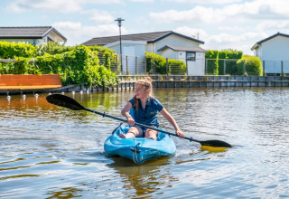 Meisje vaart met een kajak in een vakantiepark met glamping-accommodaties op een zonnige dag.