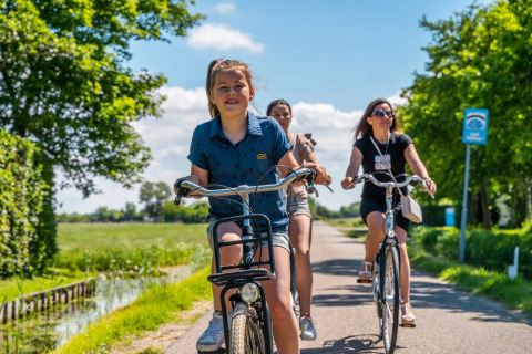 Drie personen fietsen op een zonnige dag vlakbij een vakantiepark met glamping accommodaties.