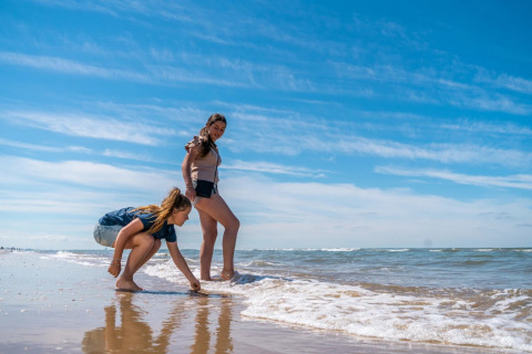 Two women enjoy a sunny day at the beach near the waves at a holiday park offering glamping accommodations.