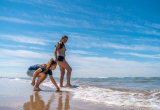 Zwei Frauen entspannen am Strand an einem sonnigen Tag in einem Ferienpark mit Glamping-Unterkünften.