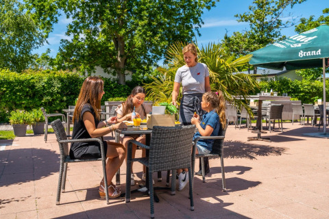 Comida al aire libre en parque vacacional con glamping, grupo disfrutando mientras camarera sirve mesa