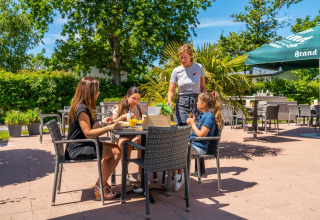 Comida al aire libre en parque vacacional con glamping, grupo disfrutando mientras camarera sirve mesa