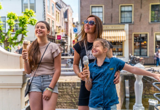 Family enjoying ice cream in the sunshine at a holiday park with glamping and charming buildings behind.