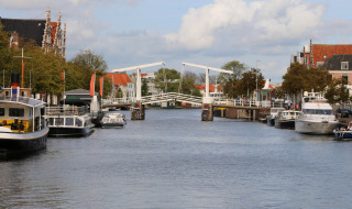 Foto de un canal con barcos y típico puente neerlandés en un parque vacacional con alojamiento glamping.