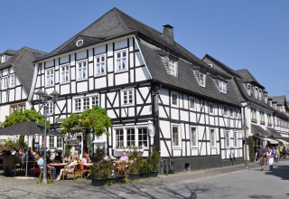 Bindingsværkshuse og udendørs café i Brilon, Nordrhein-Westfalen, Tyskland, under en klar blå himmel.