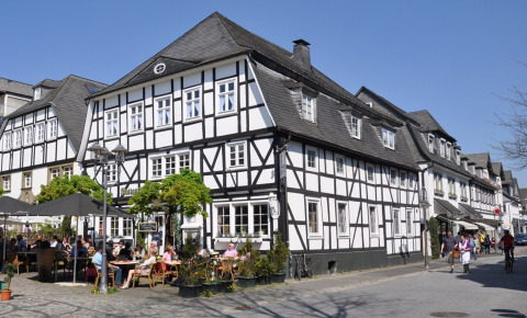 Bindingsværkshuse og udendørs café i Brilon, Nordrhein-Westfalen, Tyskland, under en klar blå himmel.