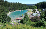 View of swimming lake and sunbathers at Camping & Ferienpark Brilon, surrounded by forest in Germany.