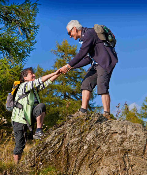 Two hikers assist each other while climbing a rock at Camping & Ferienpark Brilon holiday park, Germany.