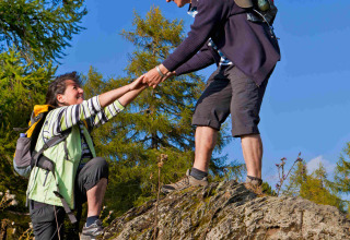 Two hikers assist each other while climbing a rock at Camping & Ferienpark Brilon holiday park, Germany.