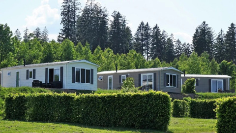 Holiday cottages with hedges and forest backdrop at Camping & Ferienpark Brilon in North Rhine-Westphalia, Germany.
