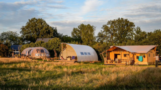 Luksus glamping telte på Holiday Park Mölke i Holland omgivet af natur og træer i solnedgangen.