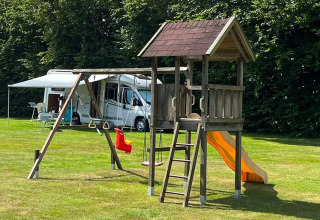 Speelplein met schommels, glijbaan en klimtoren bij een camper op gras in Drenthe, Nederland.