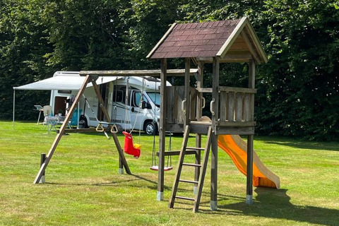 Spielplatz mit Rutsche, Schaukel und Kletterturm auf einem grünen Campingplatz in Drenthe, Niederlande.