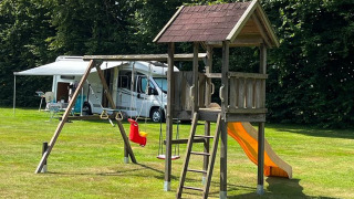 Parque infantil con columpios, tobogán y torre de madera en un camping verde en Drenthe, Países Bajos.