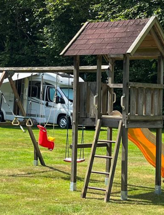 Parque infantil con columpios, tobogán y torre de madera en un camping verde en Drenthe, Países Bajos.