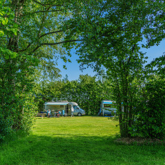 Camping verde con caravanas y personas relajándose, rodeado de árboles en Mini Camping Drentse Monden, Drenthe.