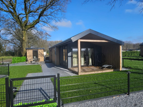 Moderne houten bungalow met overdekte veranda en omheinde tuin in Drentse Weelde vakantiepark, Drenthe, Nederland.