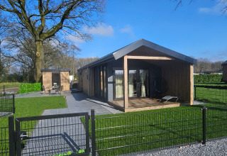 Modern wooden cabin with a covered porch and fenced yard at Drentse Weelde holiday park in Drenthe, Netherlands.