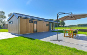Moderne feriebolig med træfacade og terrasse med spisebord under parasol i Drentse Weelde, Drenthe.