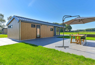 Modern holiday home with wood exterior and patio seating with umbrella at Drentse Weelde, Drenthe, Netherlands.