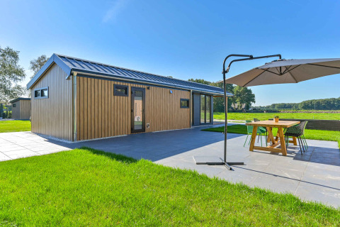 Modernes Ferienhaus mit Holzverkleidung und Terrasse mit Esstisch und Sonnenschirm in Drentse Weelde.
