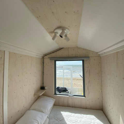 Cabaña de playa de madera con cama y ventana, vista al mar y la playa de Zeeland, Países Bajos.