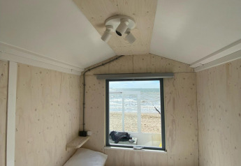 Interno di una cabina sulla spiaggia con letto e finestra che dà sul mare e la sabbia di Zeeland, Paesi Bassi.