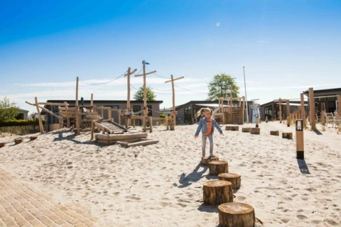Kind spielt auf einem Holzspielplatz mit Sand in einem Ferienpark mit Glamping-Unterkünften bei Sonne.