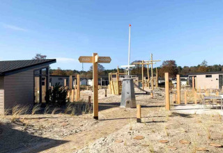 Vakantiepark met glampingaccommodaties, zandgrond, speeltuin en bord met 'Zuid' en 'Noord'.