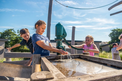 Kinderen spelen met een waterpomp op een buitenspeeltuin tijdens een zonnige dag op een glamping vakantiepark.