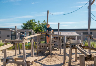 Barn leger på en legeplads med træstrukturer i et feriecenter med glampingfaciliteter og solskin.