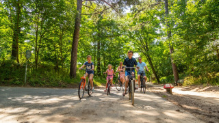 Famiglia in bicicletta lungo un sentiero forestale in un villaggio vacanze che offre sistemazioni glamping.