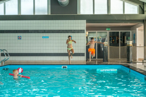 Kids jump into an indoor swimming pool at a holiday park offering glamping accommodations and play in water.