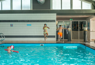 Børn hopper i en indendørs pool på et feriecenter med glampingmuligheder, mens et barn leger i vandet.