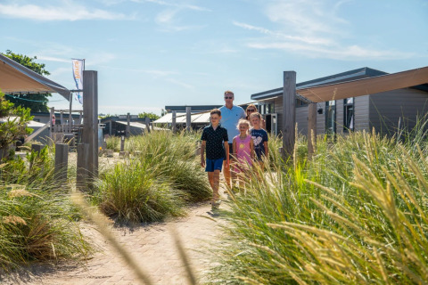 Gezin wandelt op een pad tussen hoog gras bij moderne glamping-accommodaties in een vakantiepark.