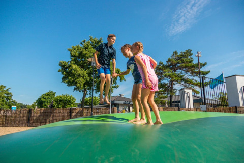 Tres niños saltan en una almohada inflable en un parque de vacaciones con alojamiento glamping soleado.
