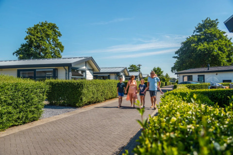 Gezin wandelt door een vakantiepark met glamping-accommodaties en groene hagen op een zonnige dag.