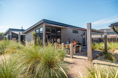 Gezin ontspant buiten bij een moderne glamping accommodatie op een zonnig vakantiepark met gras.