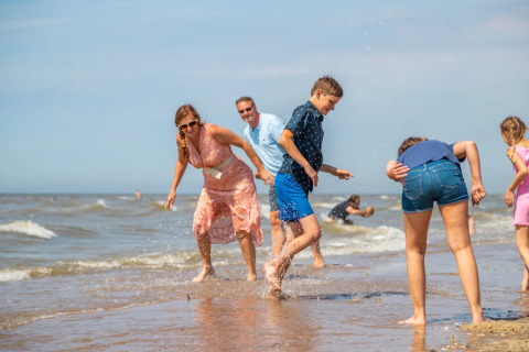 Gezin speelt vrolijk en spettert op het strand tijdens een glampingvakantie aan zee in een vakantiepark.