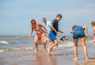 Familie leger glad sammen på en strand ved havet, mens solen skinner under et ferieophold med glamping.