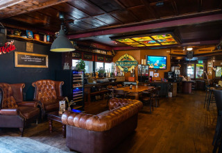 Cozy lounge area with leather sofas and bar in a holiday park glamping site, wooden décor and lighting.