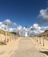Ampio sentiero tra le dune verso un faro bianco, location ideale per glamping vicino al mare.