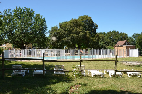 Piscina al aire libre con valla blanca y tumbonas en Camping le Roc, Occitania, Francia, rodeada de césped.