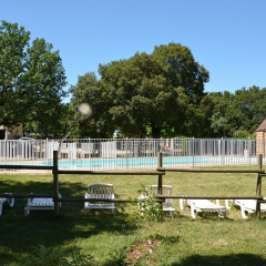 Piscina al aire libre con valla blanca y tumbonas en Camping le Roc, Occitania, Francia, rodeada de césped.