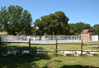 Außenpool mit weißen Liegestühlen und Zaun im Camping le Roc, Occitanie, Frankreich, an einem sonnigen Tag.