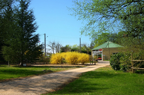 Eingang zu Camping le Roc in Okzitanien, Frankreich, mit grünen Bäumen und gelben Büschen im Frühling.