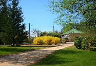 Ingresso del Camping le Roc in Occitania, Francia, con alberi verdi e cespugli gialli, cielo sereno.