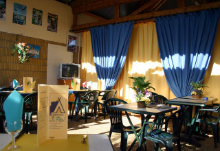 Sala da pranzo interna di Camping le Roc in Occitania, Francia, con tende blu e decorazioni floreali.