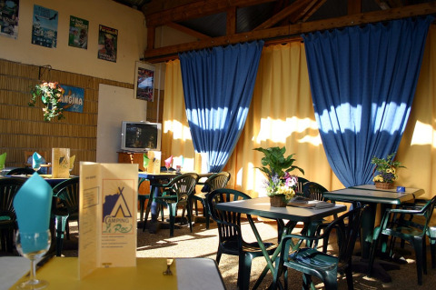Knusse eetzaal van Camping le Roc in Occitanië, Frankrijk, met blauwe gordijnen en kleurrijke decoratie.